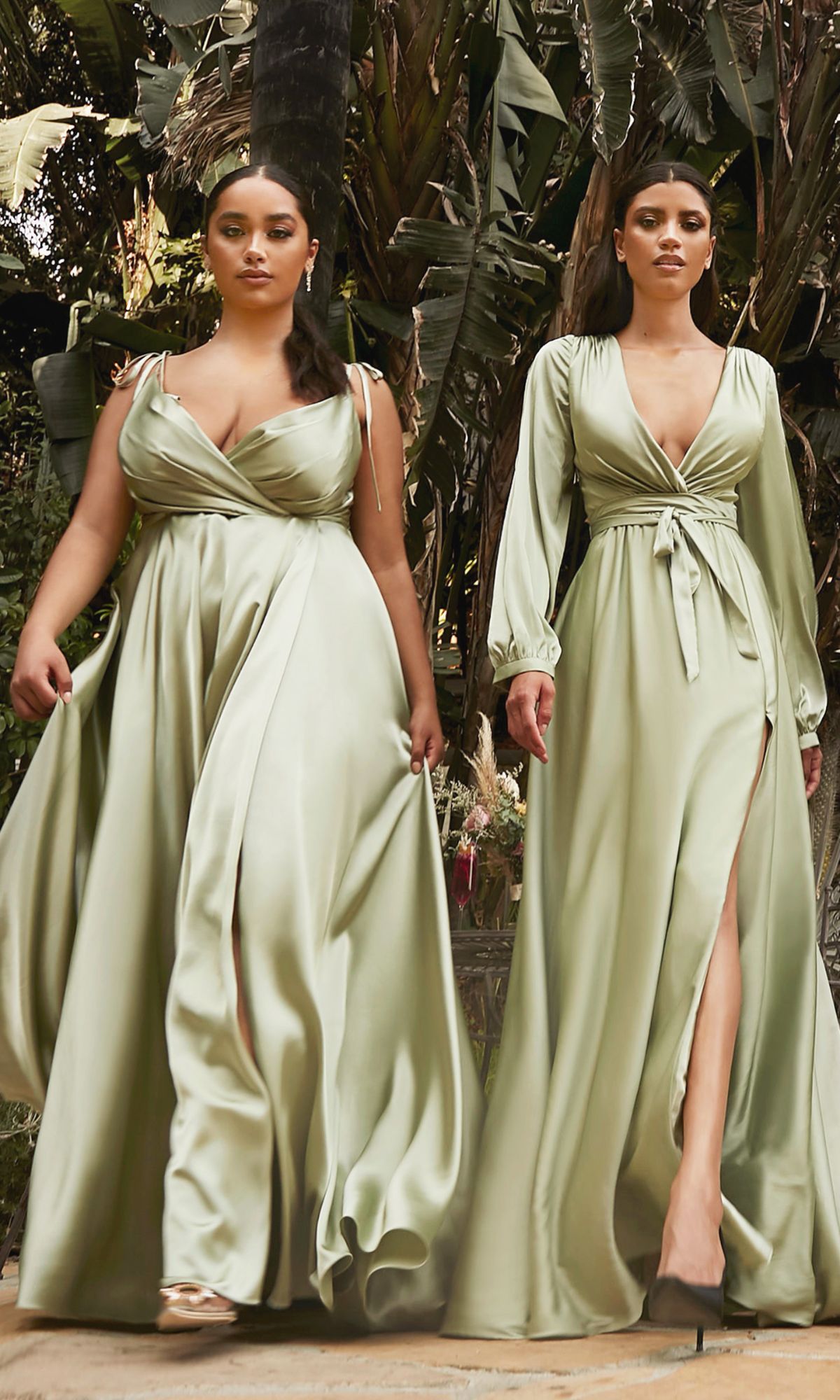 Two women wear Shoulder-Tie Long Satin V-Neck Prom Dress BD105 in light green, featuring thigh-high slits, as they walk outdoors among lush tropical plants.